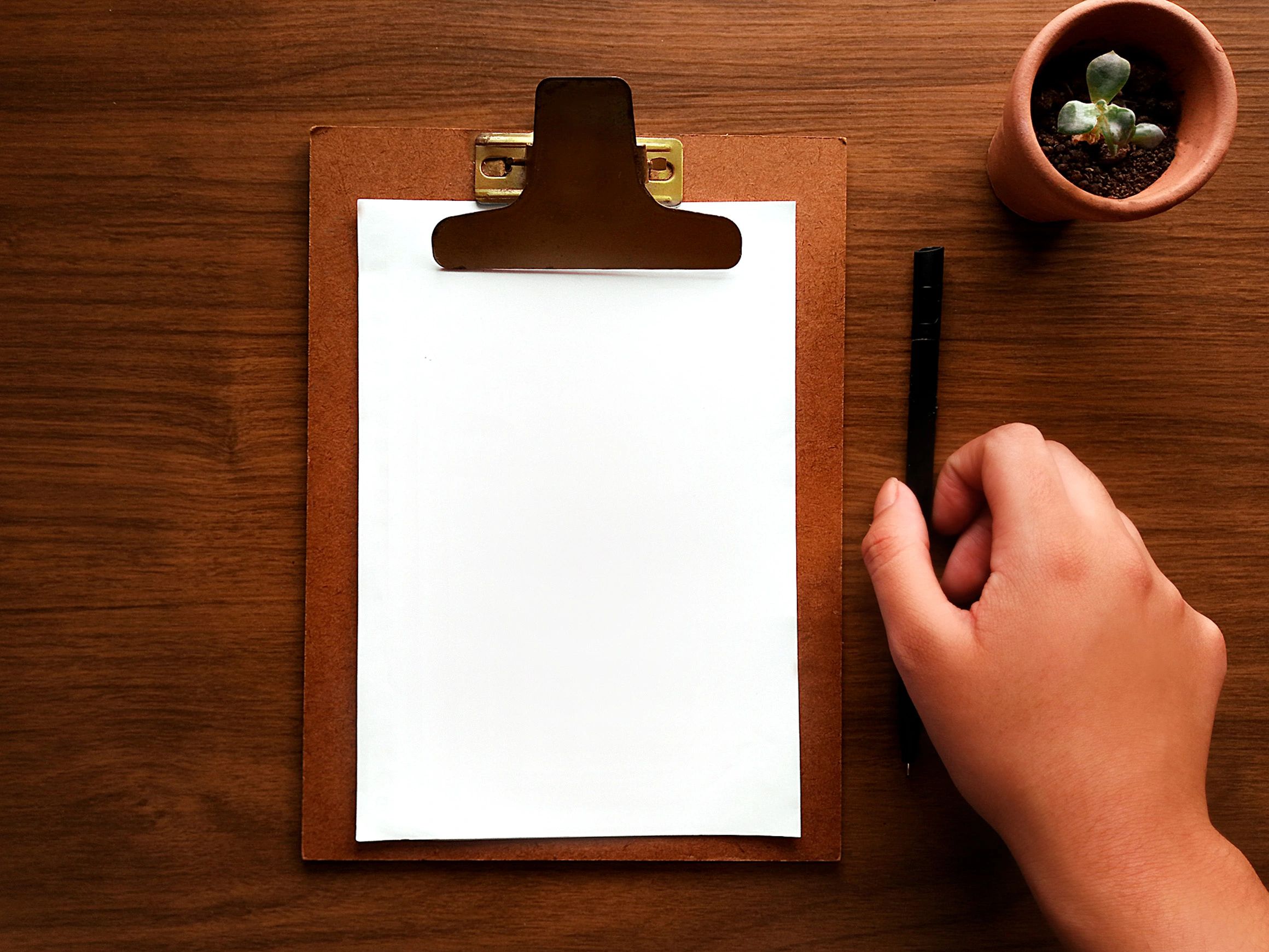 Clipboard and pen on a wooden desk representing the writing process